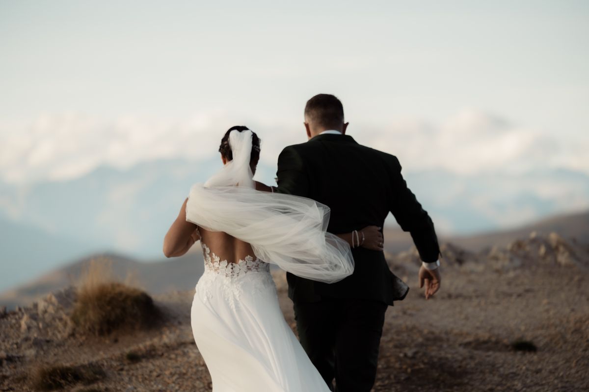 Couple walking arm in arm along a ridge, the veil blowing