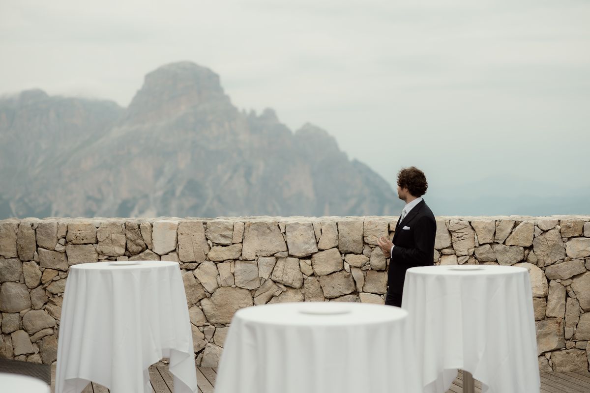 Groom by a stone wall facing the mountains
